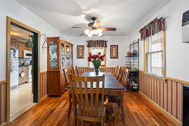 dining room with light wood-style flooring, ceiling fan, and a wainscoted wall