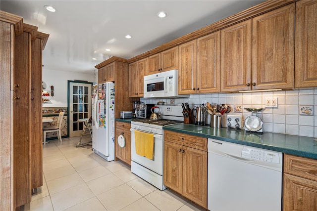 kitchen featuring white appliances, dark countertops, light tile patterned floors, and brown cabinets