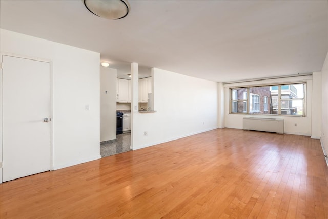 70-20 108th St Unit 15A, Forest Hills, NY 11375 - unfurnished living room featuring light wood-style floors, baseboards, and radiator heating unit