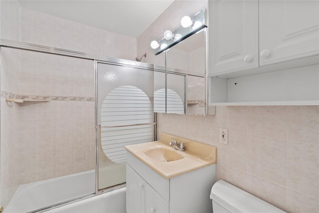 bathroom featuring tile walls, toilet, enclosed tub / shower combo, vanity, and decorative backsplash