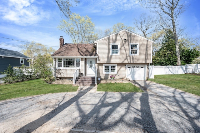 tri-level home with a chimney, fence, an attached garage, a front yard, and aphalt driveway