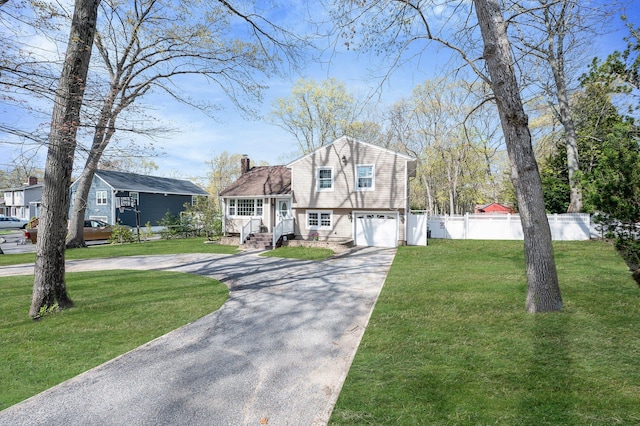tri-level home with fence, an attached garage, a front lawn, a chimney, and curved driveway