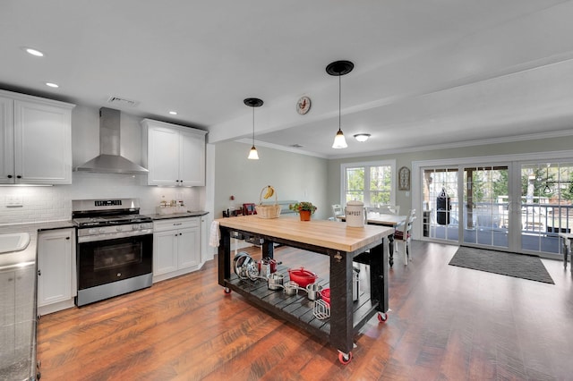 kitchen with wall chimney range hood, wood finished floors, stainless steel range with gas stovetop, and ornamental molding