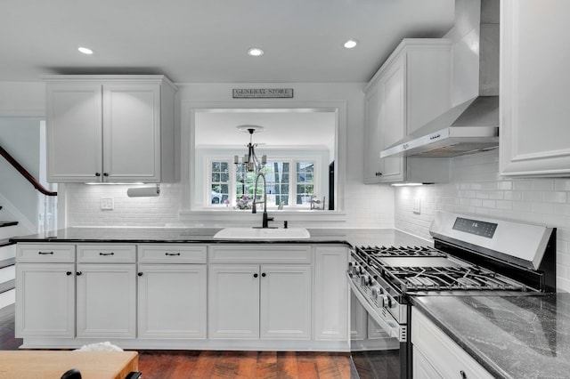 kitchen featuring a sink, stainless steel gas range oven, white cabinets, and wall chimney exhaust hood
