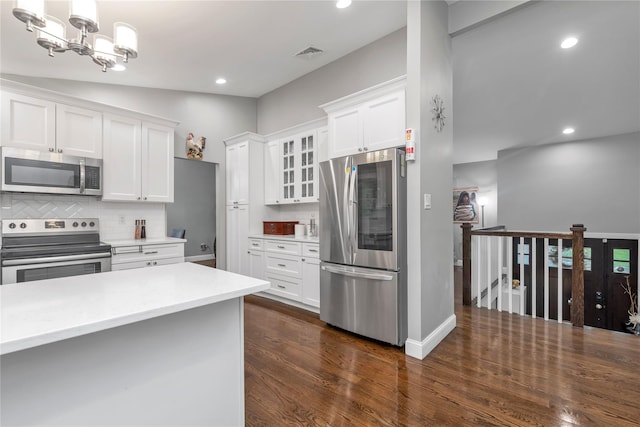 kitchen with appliances with stainless steel finishes, white cabinets, tasteful backsplash, dark wood-type flooring, and glass insert cabinets