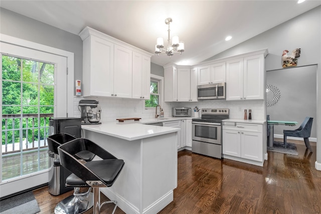 kitchen with stainless steel appliances, a chandelier, a peninsula, white cabinetry, and vaulted ceiling