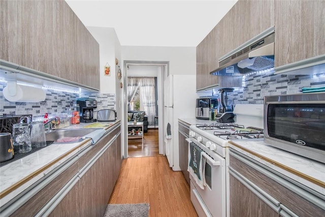 kitchen with a sink, white range with gas cooktop, under cabinet range hood, decorative backsplash, and light countertops