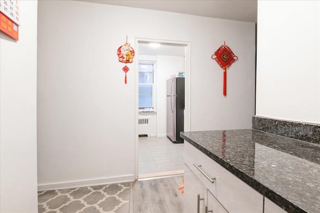hallway featuring light wood finished floors, baseboards, and radiator heating unit