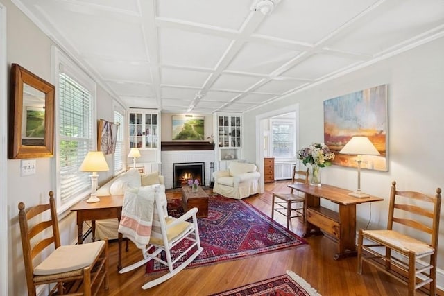 living room featuring wood finished floors, a brick fireplace, coffered ceiling, and built in features