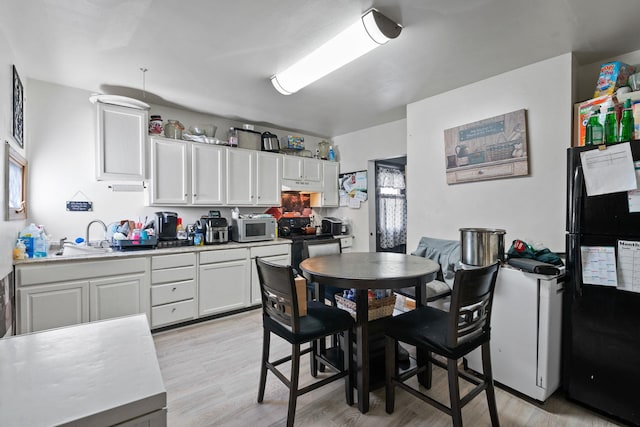 kitchen featuring a sink, white cabinets, light wood-type flooring, black appliances, and light countertops