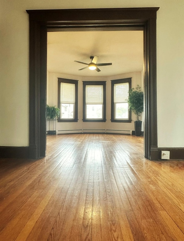 unfurnished living room with ceiling fan, baseboard heating, and hardwood / wood-style floors