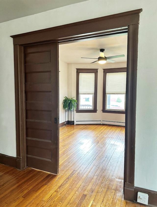 spare room with light wood-style floors, ceiling fan, baseboards, and a baseboard heating unit