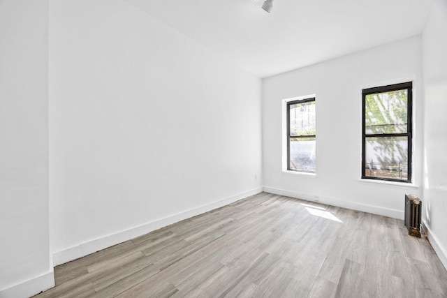 unfurnished room featuring baseboards, radiator, and light wood-style flooring