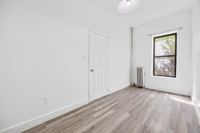 unfurnished room with baseboards, light wood finished floors, and radiator heating unit