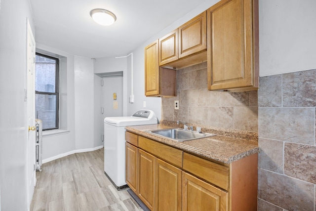 kitchen with a sink, light wood-type flooring, baseboards, backsplash, and washer / dryer