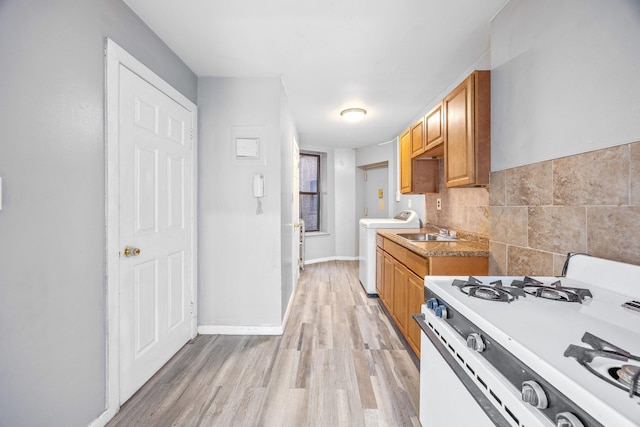 kitchen featuring white range with gas stovetop, washer / clothes dryer, baseboards, a sink, and light wood-type flooring
