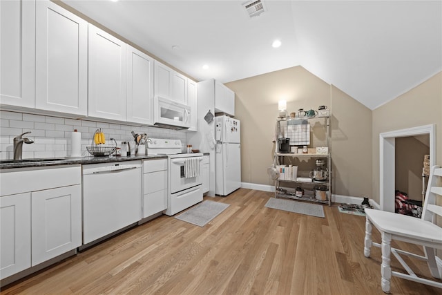kitchen featuring white appliances, a sink, dark countertops, vaulted ceiling, and light wood-style floors