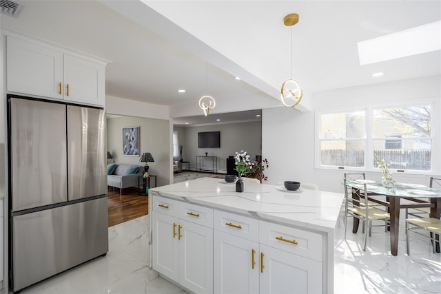 kitchen featuring freestanding refrigerator, a skylight, a kitchen island, white cabinets, and light stone countertops
