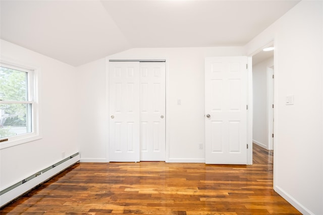 unfurnished bedroom featuring baseboard heating, wood finished floors, vaulted ceiling, a closet, and baseboards