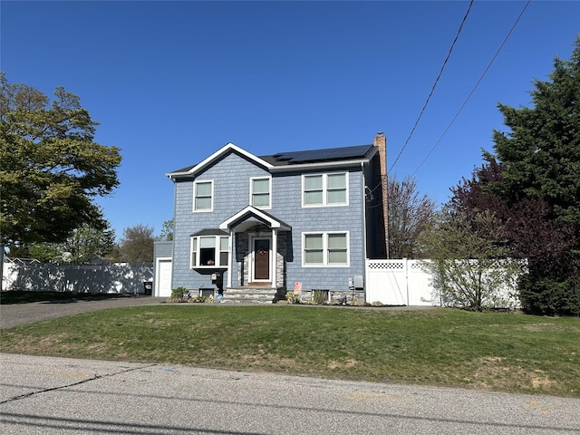 view of front of home with a chimney, fence, solar panels, aphalt driveway, and a front lawn