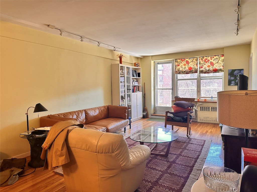 living area with wood finished floors, track lighting, and radiator heating unit