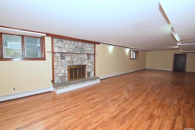 unfurnished living room with wood finished floors, baseboards, and a stone fireplace