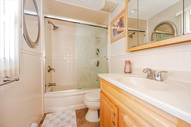 bathroom featuring wainscoting, vanity, toilet, and shower / bath combination with glass door