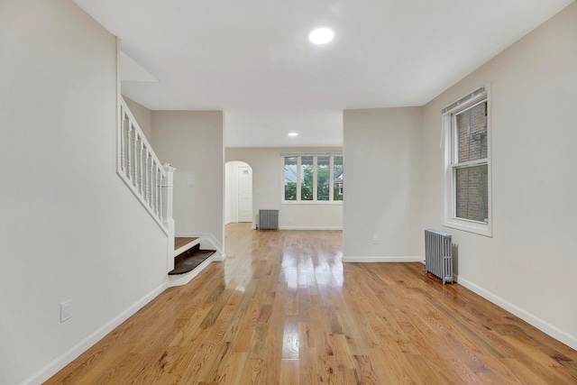 interior space featuring stairs, radiator heating unit, arched walkways, baseboards, and light wood-style floors