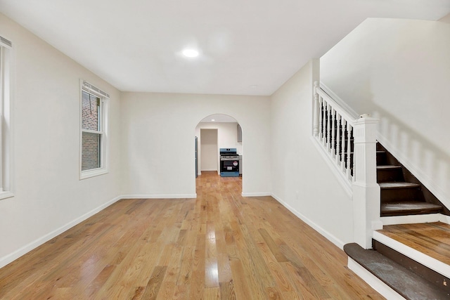 interior space featuring recessed lighting, baseboards, stairs, arched walkways, and light wood-type flooring