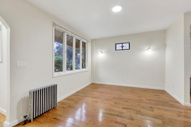 empty room with light wood-style flooring, radiator, arched walkways, and baseboards
