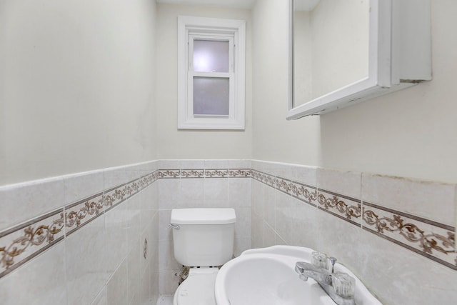 bathroom with toilet, tile walls, a sink, and a wainscoted wall