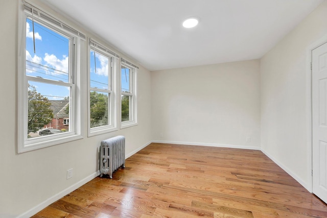 unfurnished room with radiator, light wood-type flooring, and baseboards