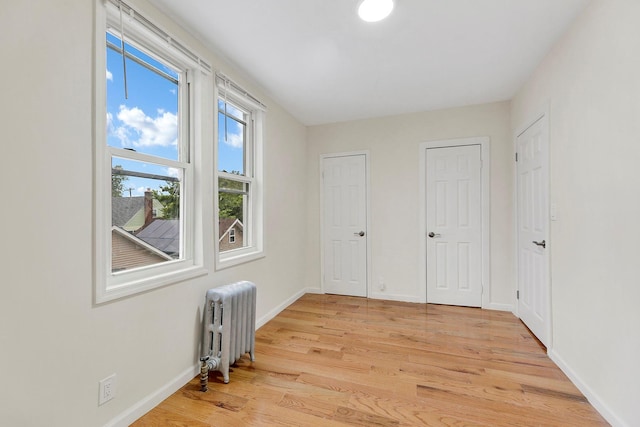 unfurnished bedroom featuring two closets, light wood-style flooring, baseboards, and radiator heating unit