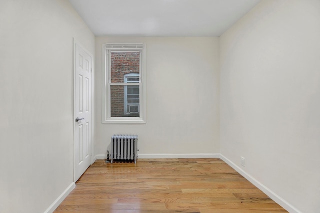 spare room featuring light wood-style floors, baseboards, and radiator heating unit