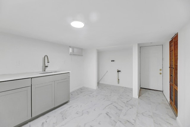 interior space featuring a sink, marble finish floor, light countertops, gray cabinetry, and baseboards