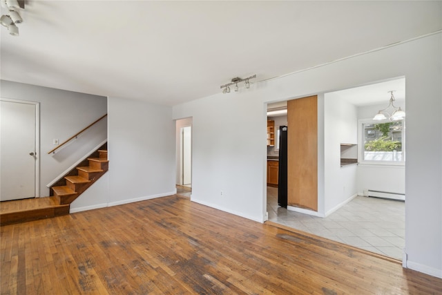 unfurnished living room featuring stairway, a baseboard heating unit, hardwood / wood-style floors, a chandelier, and rail lighting