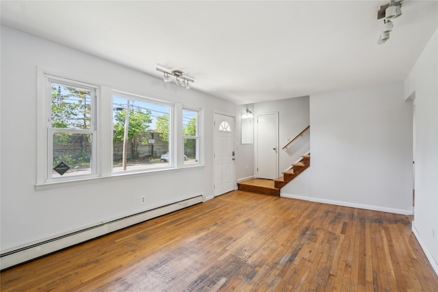unfurnished living room featuring baseboard heating, wood-type flooring, plenty of natural light, and stairs