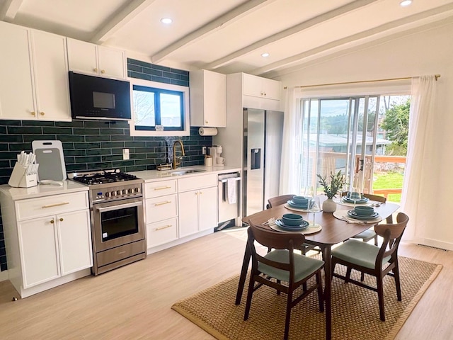 kitchen with appliances with stainless steel finishes, a sink, decorative backsplash, light wood-style floors, and plenty of natural light