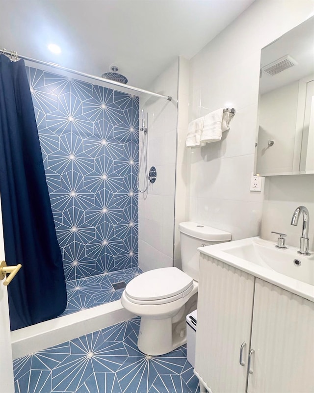 bathroom featuring toilet, a stall shower, tile patterned flooring, vanity, and tile walls