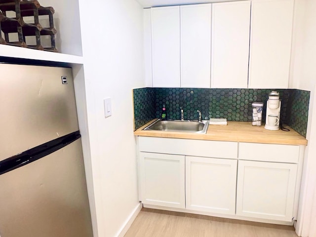 bar area featuring freestanding refrigerator, a sink, backsplash, light wood-style flooring, and baseboards