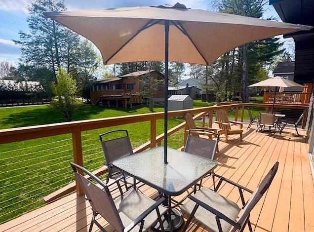 deck with outdoor dining area, a storage shed, an outbuilding, and a lawn