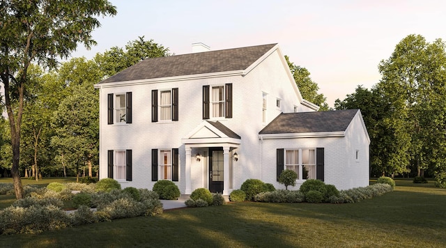colonial home with a chimney, a shingled roof, brick siding, and a front lawn