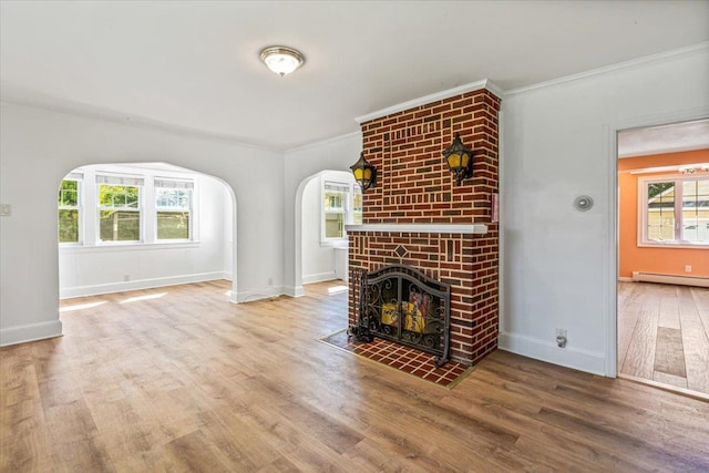 unfurnished living room featuring arched walkways, ornamental molding, baseboards, and wood finished floors