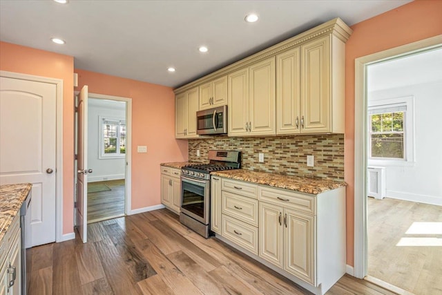 kitchen with stainless steel appliances, cream cabinetry, decorative backsplash, and light wood-style flooring