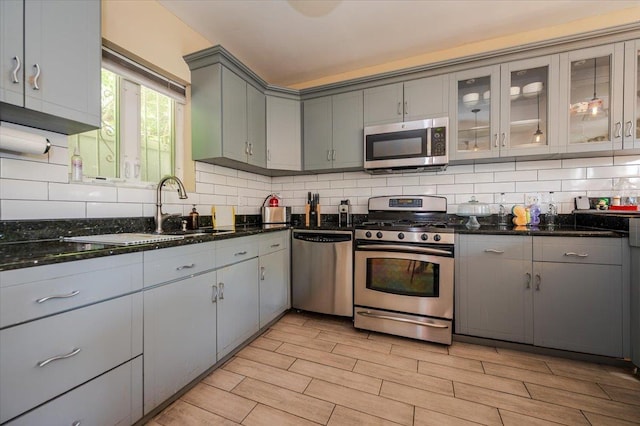 kitchen with a sink, gray cabinets, wood finish floors, appliances with stainless steel finishes, and tasteful backsplash