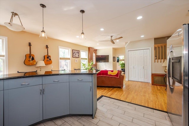kitchen with light wood-style flooring, a wealth of natural light, stainless steel fridge with ice dispenser, and dark countertops