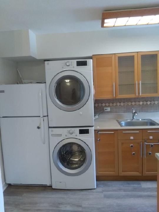 laundry room with estacked washer and dryer, a sink, and light wood-style floors