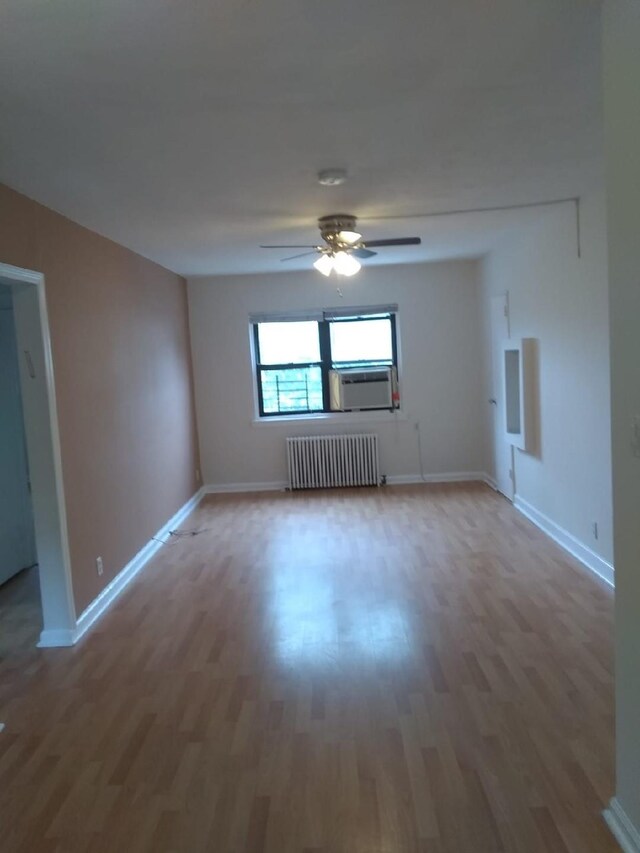 spare room with radiator heating unit, wood finished floors, cooling unit, ceiling fan, and baseboards