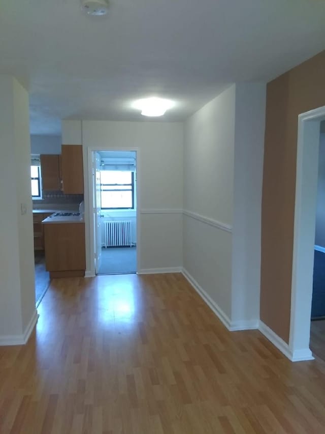 unfurnished dining area with radiator heating unit, light wood finished floors, and baseboards
