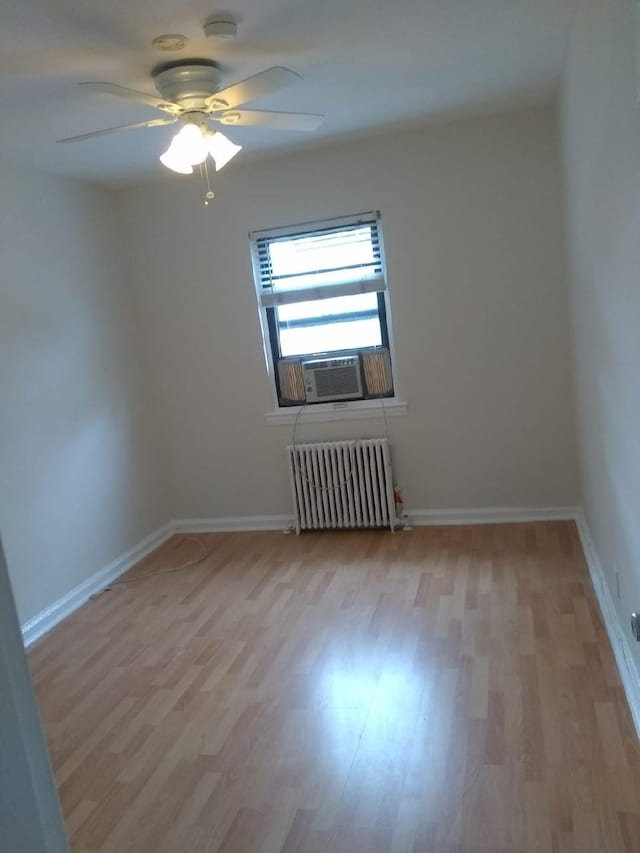 spare room featuring radiator heating unit, light wood finished floors, ceiling fan, cooling unit, and baseboards